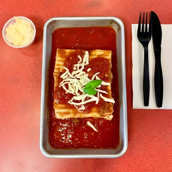 King's Pizza lasagna in a metal pan with tomato sauce, cheese, basil, and a side of parmesan.