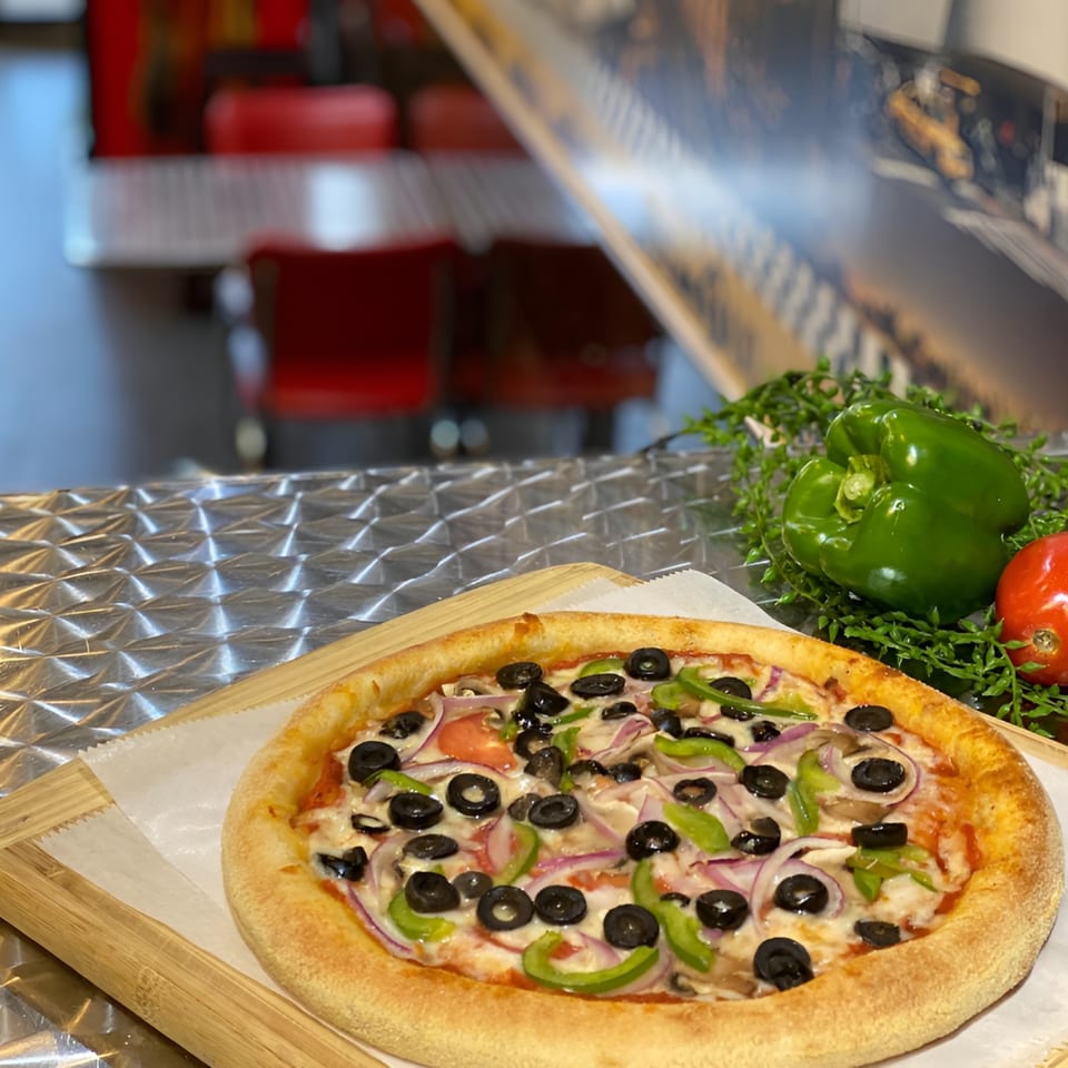 King's Pizza veggie pizza with olives, peppers, onions, and mushrooms on a wooden board.