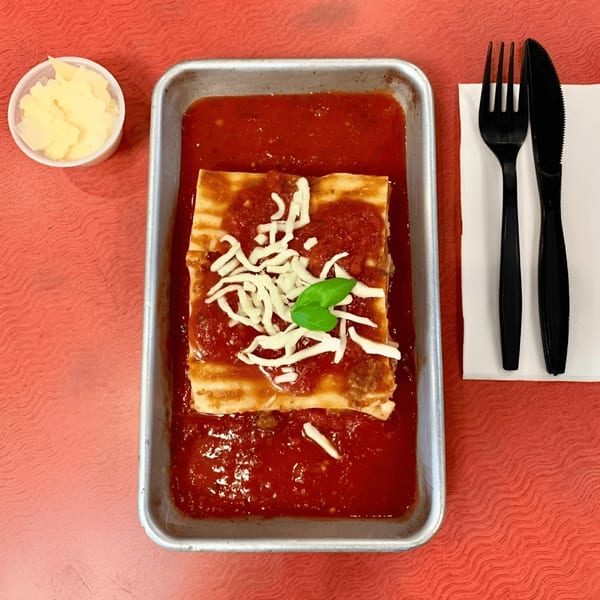 King's Pizza lasagna in a metal tray with tomato sauce, shredded cheese, and basil.