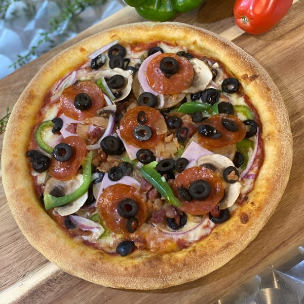 King's Pizza's supreme pizza with pepperoni, olives, mushrooms, onions, and green peppers on a wooden board.